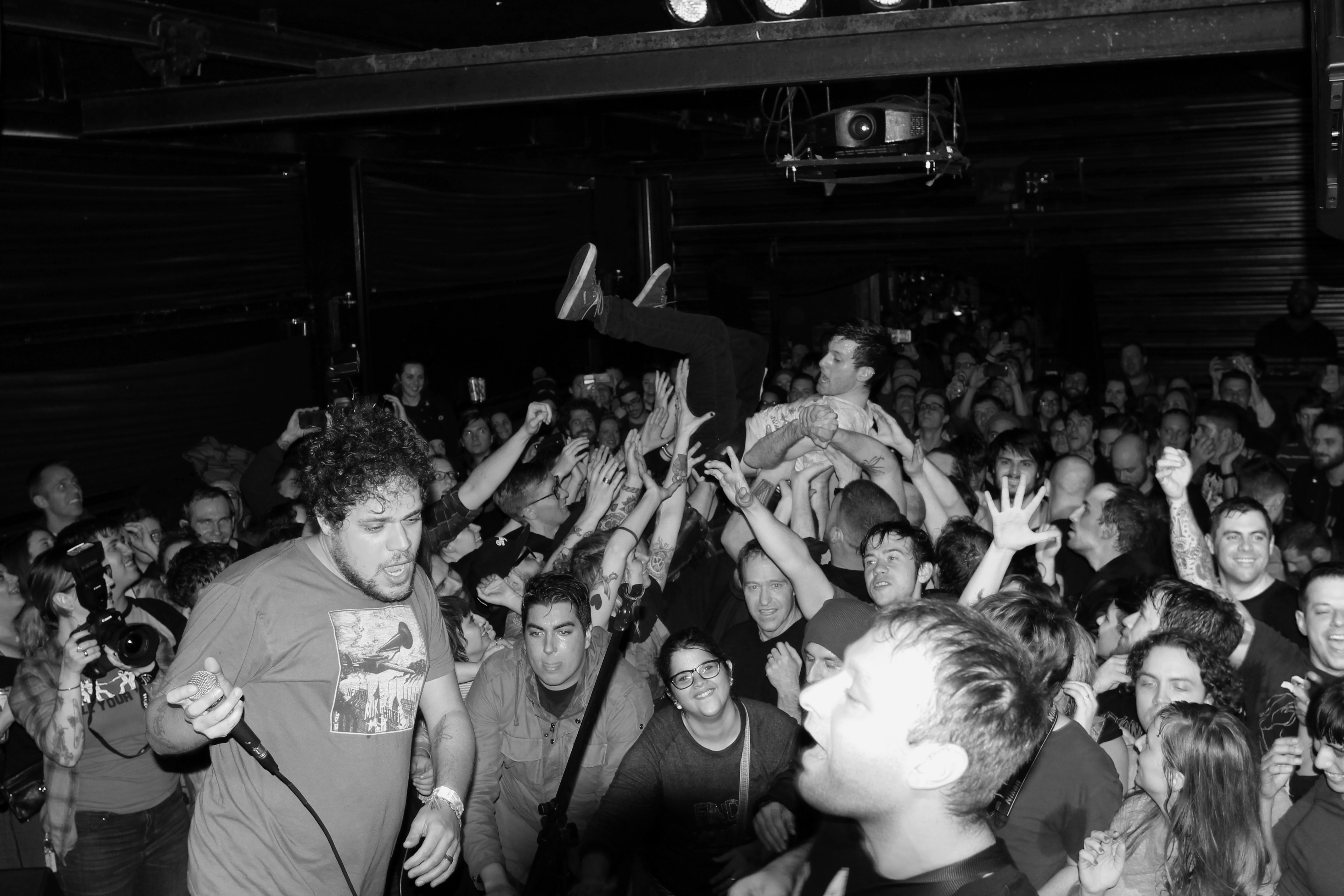 jeff rosenstock holds a microphone on stage while pup lead singer stefan babcock crowdsurfs over the excited masses at st. vitus. photo by killian young.